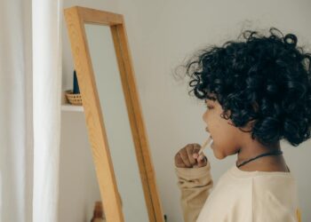 Young child with curly hair brushing teeth in front of mirror, emphasizing morning routine and hygiene.
