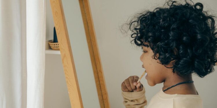 Young child with curly hair brushing teeth in front of mirror, emphasizing morning routine and hygiene.